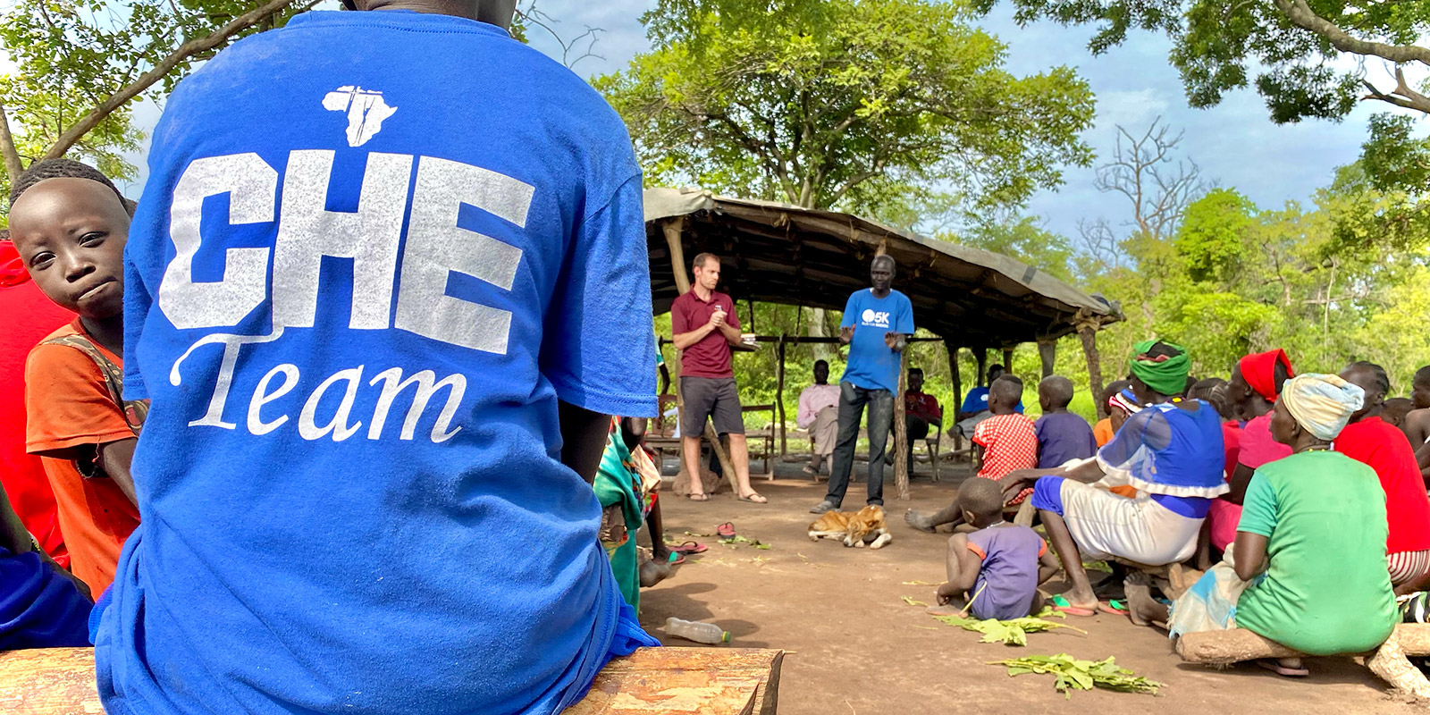 Crowd listening to two men teach. A person with a CHE team t-shirt sits in the foreground.