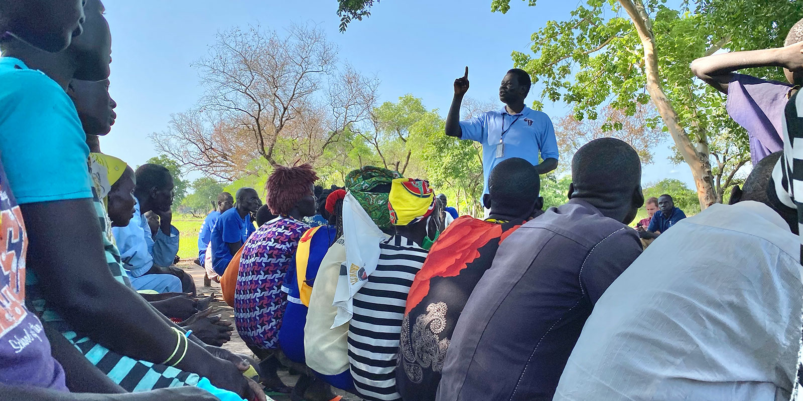 Crowd in village listening to man in In Deed And Truth shirt teaching.