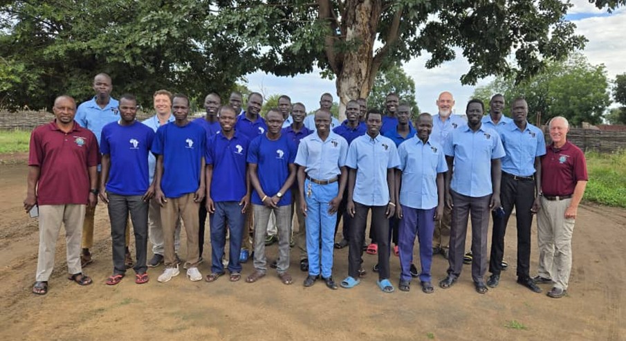 Michael with IDAT Pastors in Tonj posing for a photo in front of a tree