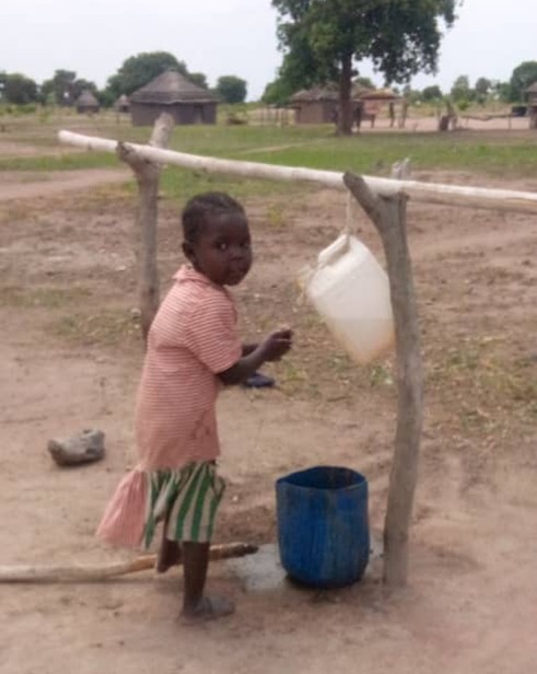 A Child in the Village using a Tippy Tap, a white jug filled with water that has with small holes in the cap.