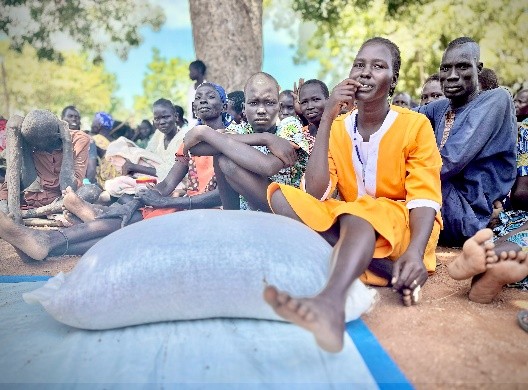A group of people sitting on the ground.  A bag of food in the foreground.