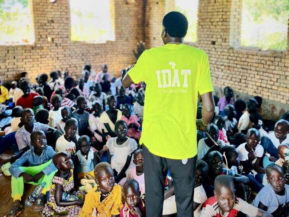 A person in a yellow shirt speaking to a group of people