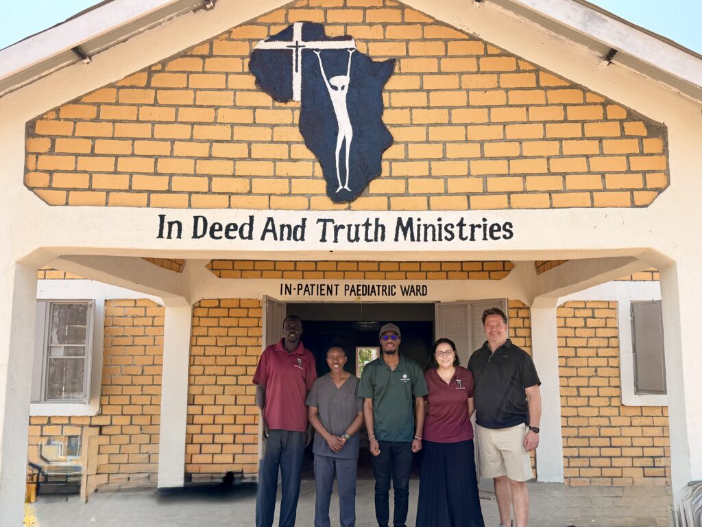 Photograph of five people standing in front of a brick building labeled 