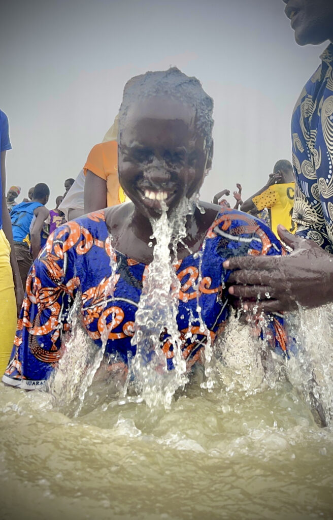 A person rising out of the water.  Water flowing off her face and chlothing